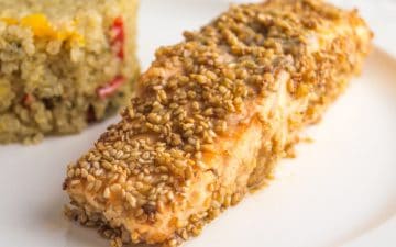 zoomed image of a salmon fillet with sesame seeds, with quinoa side on the background