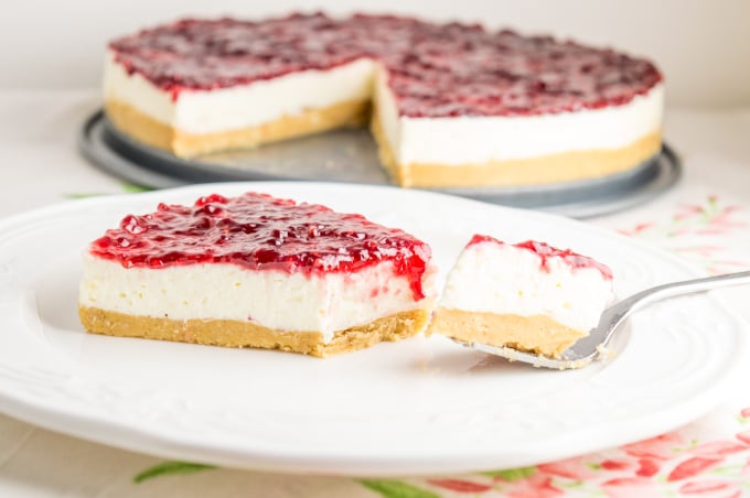 a slice of raspberry cheesecake cut with a fork, with the rest of the cake on the background.