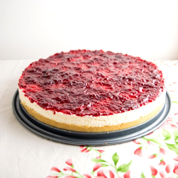 A cheesecake covered with raspberry jam, on a flower tablecloth
