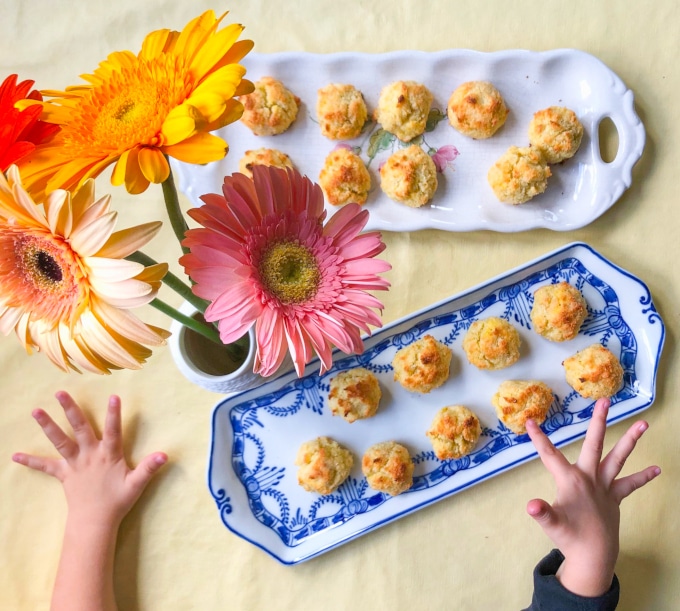 Two platters with coconut macaroons, kid's hands pointing at them, on a table decorated with flowers