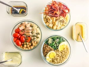 três bowls redontos com saladas e três recipientes rectangulares com molhos