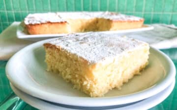 pormenor de uma fatia de bolo de limão low fodmap num prato com bolo ao fundo