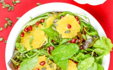 salada festiva e molho de salada numa mesa vermelha com semenets de abóbora espalhadas