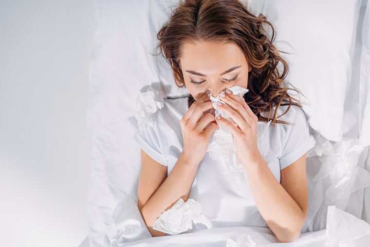 rapariga com gripe ou constipação na cama a assiar o nariz